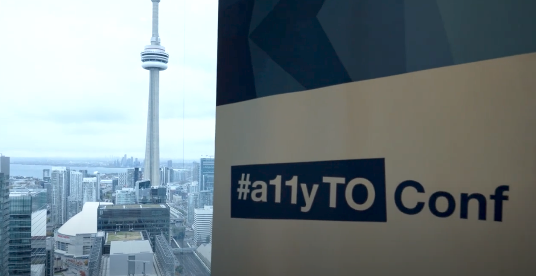 A photograph taken from Microsoft at CIBC Square. On the left side in the background features the CN Tower, while the right side in the foreground shows one of our vertical banners branded with our Conf logo.