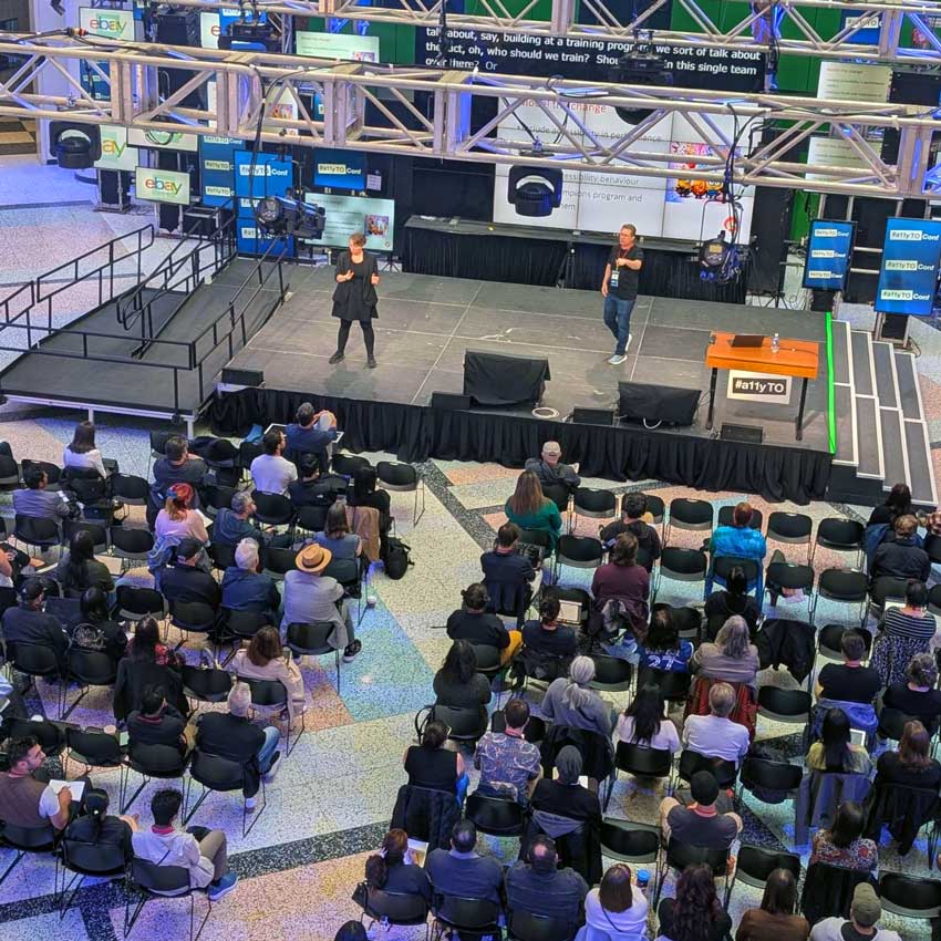 The CBC Barbara Frum Atrium stage, shot from above, during a Conf 2025 presentation with a speaker and an interpreter in front of attendees